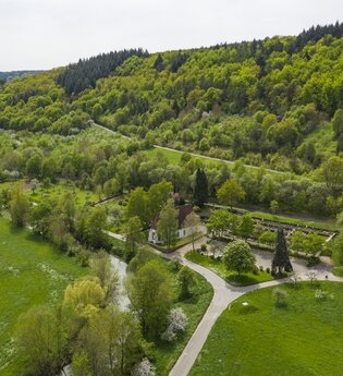 Luftbildaufnahem auf einen Parkplatz/Wohnmobilstellplatz bei Distelhausen. Daneben ist eine Kapelle und ein Friedhof zu sehen.  Es ist ein idyllischer Ort an der Tauber, mit Wiesen und bewaldeten Hügeln. | © Tourist-Info Tauberbischofsheim