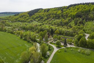 Luftbildaufnahem auf einen Parkplatz/Wohnmobilstellplatz bei Distelhausen. Daneben ist eine Kapelle und ein Friedhof zu sehen.  Es ist ein idyllischer Ort an der Tauber, mit Wiesen und bewaldeten Hügeln. | © Tourist-Info Tauberbischofsheim