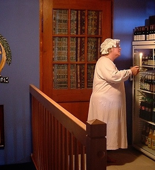 Eine Peson steht in Nachthemd und Mütze vor einem Kühlschrank mit Getränken | © Touristikgemeinschaft Hohenlohe e. V.| Winklers Weinstube