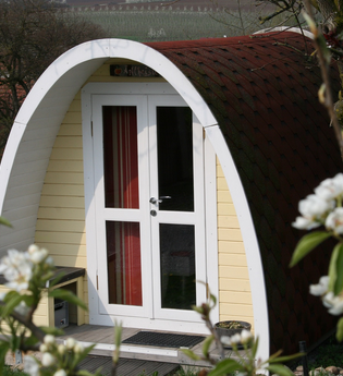 Der Campingpod von außen ist umrahmt von vielen Bäumen. | © Touristikgemeinschaft Hohenlohe e. V. | Burgstallhof