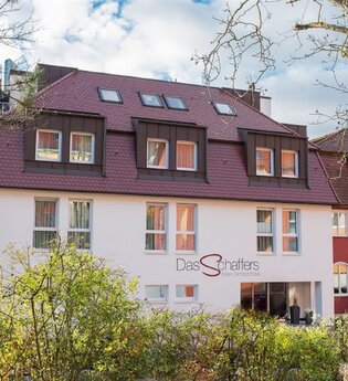 Hotel Das Schaffers mit rotem Dach und weiß-roter Fassade, umgeben von Bäumen und Sträuchern | © Das Schaffers