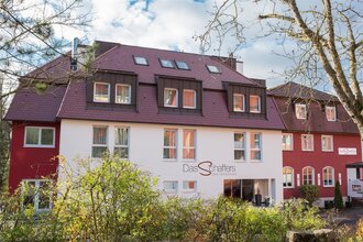 Hotel Das Schaffers mit rotem Dach und weiß-roter Fassade, umgeben von Bäumen und Sträuchern | © Das Schaffers
