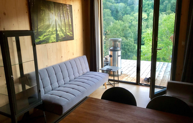 Im Wohnzimmer steht eine hellgraue Couch und die Tür geht hinaus ins Grüne | © Touristikgemeinschaft Hohenlohe e. V.| Katharina Schmieg