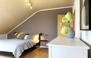 Schlafzimmer 1 der großen Ferienwohnung mit breitem Bett, dazu Nachttische und Lampen und ein kleinerer weißer Schrank am Eingang | © Neckar-Zaber-Tourismus e.V.