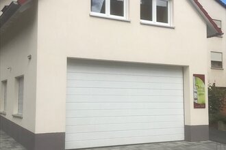 Haus mit weißer Fassade, rotem Dach und großer weißer Garagentür, Pflastersteine vor dem Haus | © Brennerei Stilling