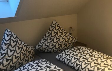 Doppelbett unter Dachschräge mit Bettwäsche in Weiß und schwarzen Herzmustern, Dachfenster links | © Brennerei Stilling