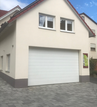 Haus mit weißer Fassade, rotem Dach und großer weißer Garagentür, Pflastersteine vor dem Haus | © Brennerei Stilling