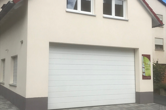 Haus mit weißer Fassade, rotem Dach und großer weißer Garagentür, Pflastersteine vor dem Haus | © Brennerei Stilling