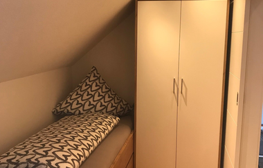 Kleines Schlafzimmer mit Dachschräge, Einzelbett mit Herz-Muster-Bettwäsche und weißem Kleiderschrank | © Brennerei Stilling
