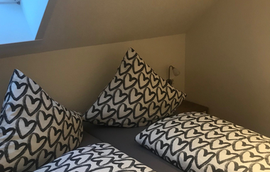 Doppelbett unter Dachschräge mit Bettwäsche in Weiß und schwarzen Herzmustern, Dachfenster links | © Brennerei Stilling