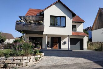 Modernes zweistöckiges Haus mit weißer Fassade, rotem Ziegeldach, Balkon mit Pflanzen und gepflasterter Einfahrt | © Simone Bürckert