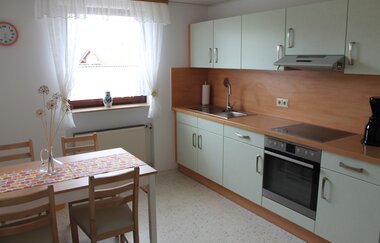Helle Küche mit Schränken, Holzarbeitsplatte, Herd, Spüle und kleinem Esstisch mit vier Stühlen und Blumenvase | © Ferienwohnung Ehrmann