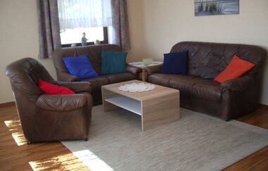 Wohnzimmer mit braunen Ledersofas, bunten Kissen, einem hellen Holztisch und einem grauen Teppich auf Holzboden | © Ferienwohnung Ehrmann