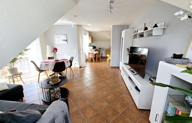 Helles Wohnzimmer mit braunem Fliesenboden, grauem Sofa, runden Esstisch mit vier Stühlen und offener Küche im Hintergrund | © Familie Fuhrmann