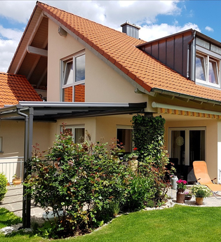 Einfamilienhaus mit rotem Ziegeldach und gepflegtem Garten bei Sonnenschein; Schlafzimmer mit Holzmöbeln und floralem Bettbezug; Wohnzimmer mit Sofa, Esstisch und moderner TV-Möbelwand. | © Familie Fuhrmann