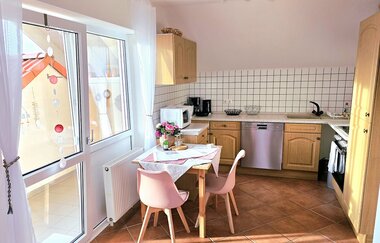 Kleine Küche mit Holzmöbeln, weiß gefliester Wand, Spülmaschine, Mikrowelle, Kaffeemaschine und kleinem Esstisch mit zwei rosa Stühlen und Blumendekoration | © Familie Fuhrmann