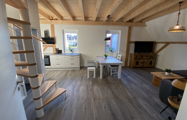 Offener Wohnbereich mit Holzdecke, Wendeltreppe, moderner Küchenzeile, Esstisch mit Stühlen und Fernseher auf Holzkommode | © Ferienwohnung Etzl