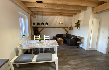 Wohn- und Esszimmer mit Holzbalkendecke, weißem Esstisch mit Bank und Stühlen, grauem Ecksofa und Holztisch | © Ferienwohnung Etzl