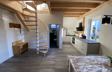Offene Wohnküche mit moderner Küchenzeile, Holzwendeltreppe mit Metallgeländer und Holzbalkendecke | © Ferienwohnung Etzl