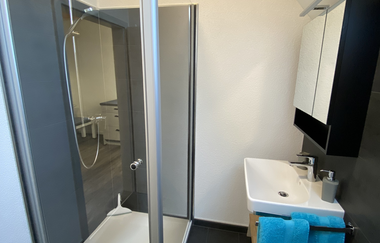 Modernes Badezimmer mit Glasdusche, weißem Waschbecken, Spiegel und zwei blauen Handtüchern | © Ferienwohnung Etzl