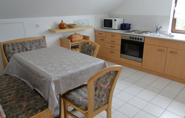 Küchenzeile mit braunen Schränken und Ofen, Herd,  Mikrowelle und Spüle. Gegenüber ein Esstisch mit zwei Sitzbänken und zwei einzelnen Stühlen | © Neckar-Zaber-Tourismus e.V.