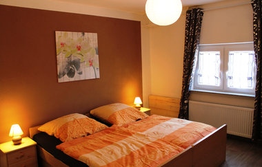 Im Schlafzimmer steht ein Doppelbett., ein Bild hängt an einer braunen Wand | © Touristikgemeinschaft Hohenlohe e. V.| Ferienwohnung Kraft