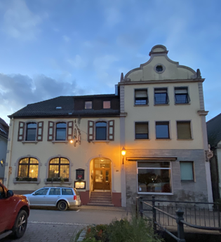 Zweistöckiges Gebäude mit geschwungenem Giebel und beleuchtetem Eingang bei Abenddämmerung, zwei geparkte Autos davor | © Ferienwohnung Etzl