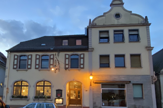 Zweistöckiges Gebäude mit geschwungenem Giebel und beleuchtetem Eingang bei Abenddämmerung, zwei geparkte Autos davor | © Ferienwohnung Etzl