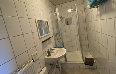 Modernes Badezimmer mit weiß gefliesten Wänden, Waschbecken, Spiegel, Duschkabine und Handtuchhalter mit blauen Handtüchern | © Ferienwohnung Etzl