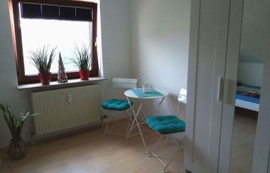 Raum mit kleinem runden Tisch und zwei Stühlen mit türkisenen Sitzkissen