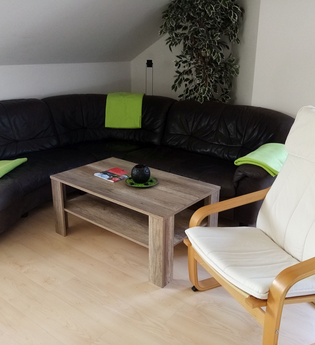 Wohnzimmer mit schwarzer Couch und Couchtisch, dazu ein Sessel