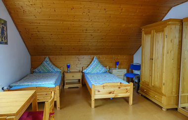 Zwei Betten im Schlafzimmer mit Nachttischschränken und einem großen Holzschrank und einem Holztisch + Stuhl | © Neckar-Zaber-Tourismus e.V.
