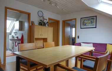 Wohnraum bestehend aus einem großen Esstisch mit vier Stühlen, einer violetten Couch und einem Schrank, jeweils eine Türe zum Badezimmer und zwei weiteren Räumen | © Neckar-Zaber-Tourismus e.V.