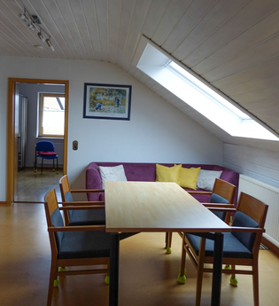 Esstisch mit vier Stühlen, eine violette Couch mit gelben und weißen Kissen und ein Holzschrank mit Deko | © Neckar-Zaber-Tourismus e.V.