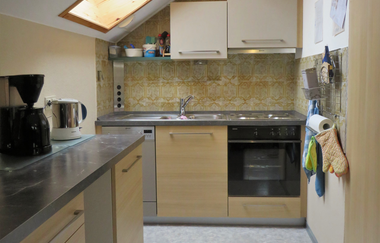 Kleine Küche mit Dachfenster, Holzschränken, grauen Arbeitsflächen, Kaffeemaschine, Wasserkocher und eingebautem Ofen