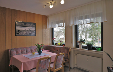 Essbereich mit rosa Tischdecke, Eckbank und Stühlen, Fenster mit weißen Gardinen und Pflanzen auf der Fensterbank