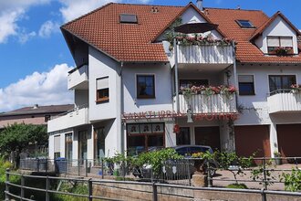 Mehrstöckiges Wohn- und Geschäftshaus mit rotem Ziegeldach und Balkonen mit Blumen, darunter die Sankt Urban Apotheke | © Ferienwohnung Roth