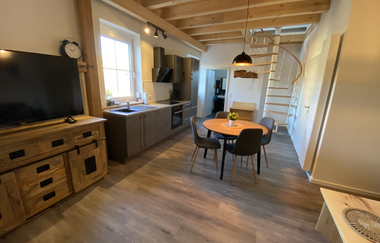 Offene Küche mit grauen Schränken, Esstisch mit vier Stühlen, Holzdecke mit sichtbaren Balken und Wendeltreppe im Hintergrund | © Ferienwohnung Etzl