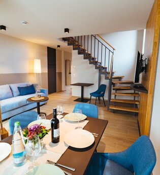 Esstisch mit mindestens 4 Stühlen, eine pastellblaue Couch, Tisch und Stuhl neben der Treppe nach oben | © Neckar-Zaber-Tourismus e.V.