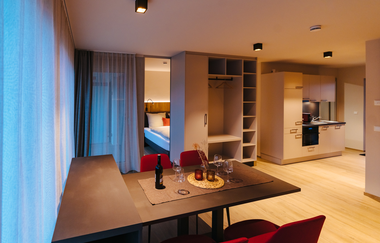 Bild der Essecke bestehend aus einem Holztisch und vier roten Stühlen, im Hintergrund sieht man das Bett, den Schrank und die Küche | © Neckar-Zaber-Tourismus e.V.