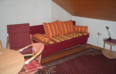 Wohnzimmer mit roter Couch und orangefarbenen Kissen, ein roter Sesselstuhl und ein Holztisch. | © Neckar-Zaber-Tourismus e.V.