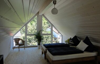 Zimmer Ferienwohnung mit Betten und Stuhl und einer dreieckigen Fensterfront | © Neckar-Zaber-Tourismus e.V.