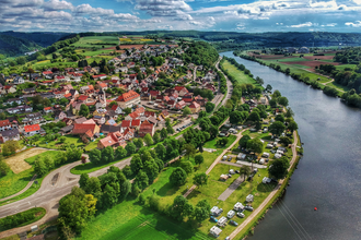 Drohnenaufnahme mit Blick auf einen Fluss (Neckar). Auf der rechten Uferseite sieht man einen Campingplatz und dahinter einen angrenzenden Ort. Binau im Odenwald. | © Fortuna Camping am Neckar
