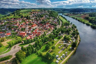 Drohnenaufnahme mit Blick auf einen Fluss (Neckar). Auf der rechten Uferseite sieht man einen Campingplatz und dahinter einen angrenzenden Ort. Binau im Odenwald. | © Fortuna Camping am Neckar