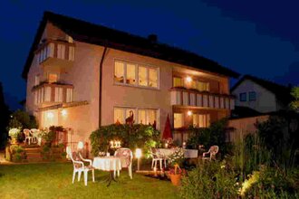 Ein großes Haus mit einem Garten, Gartenmöbel stehen dort. Es ist Abend. | © Gästehaus Marianne