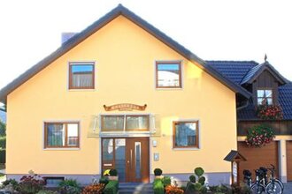 Gelbes Einfamilienhaus mit brauner Haustür, vier Fenstern und einem kleinen Garten mit Blumen. | © Gästehaus Mittnacht