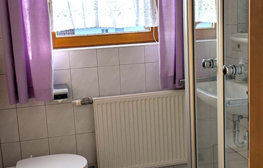 Badezimmer mit lila Vorhängen, Duschkabine und Toilette | © Bauer-Thorpe