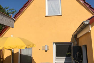 Gelbes Haus mit rotem Dach, weißer Tür, grauer Garage und Terrasse mit blauem Stuhl, gelbem Sonnenschirm und kleinem Tisch | © Gästehaus Sabine