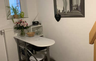 Kleiner Essbereich mit weißem Tisch, grauem Stuhl, Toaster und Radio auf Wandregal, Wellen-Spiegel und Treppe aus Holz | © Gaestehaus Sabine