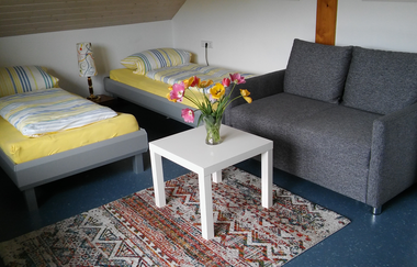 In einem Gästezimmer gibt es zwei Betten, ein Sofa und ein Beistelltisch. | © Touristikgemeinschaft Hohenlohe e. V. | Ferienwohnung / Gästehaus Heßlinger